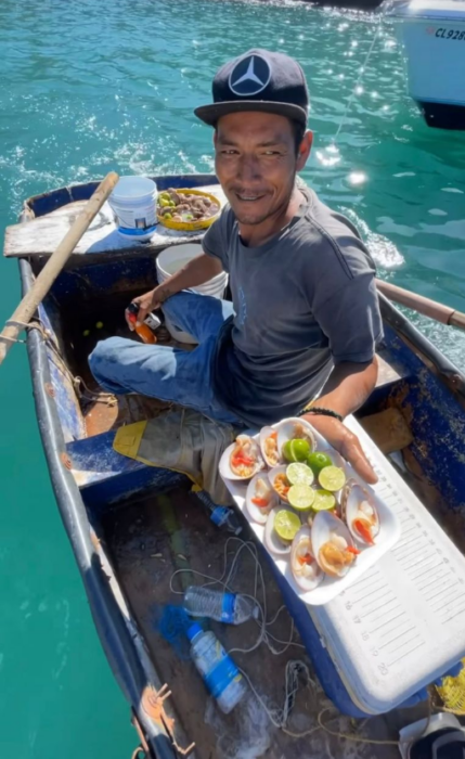 un sencillo pescador ofrece un plato de almejas con limones subido en su lancha y en pleno mar