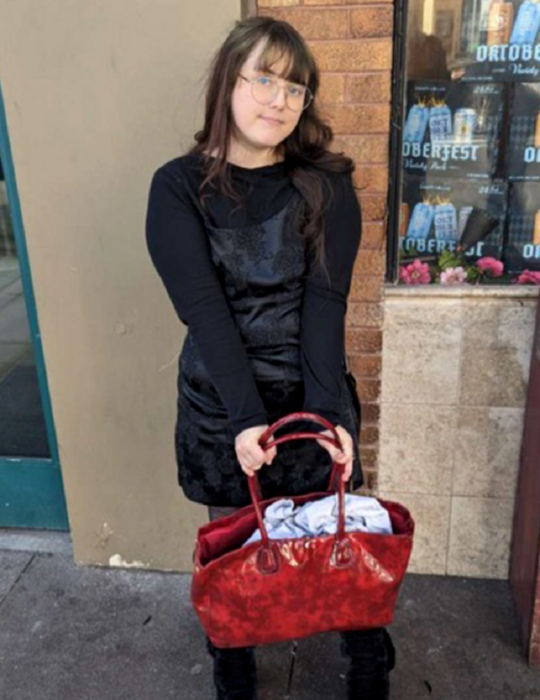 una chica posa para la cámara vestida de negro y con una bolsa grande roja como accesorio 