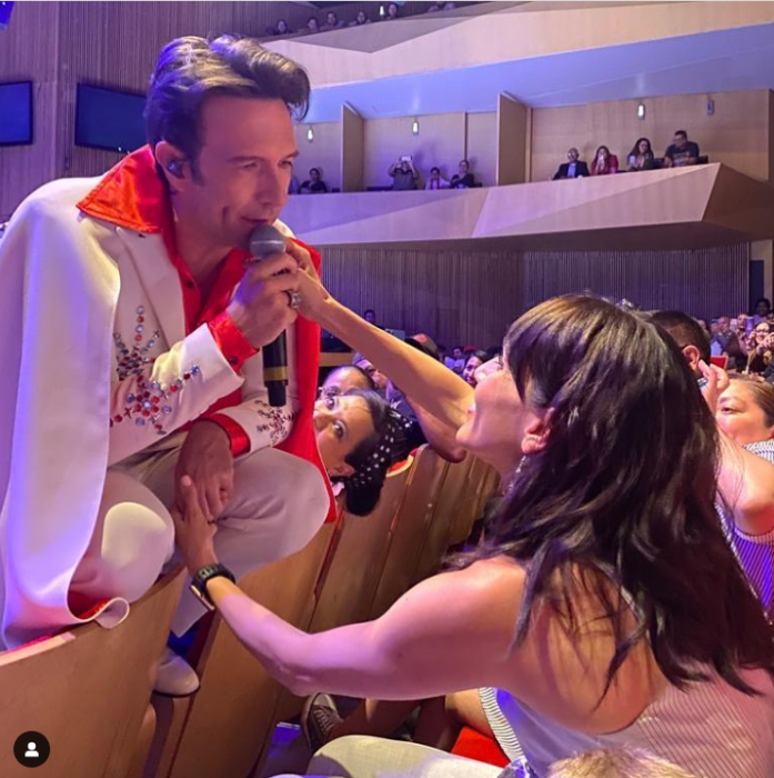 Sandra Echeverría y Leonardo de Lozanne caracterizado como Elvis Presley canta sobre las butacas para tomar de la mano a su esposa que está sentada