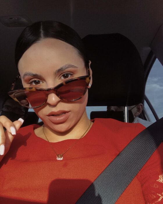 Selfie de una chica vestida de rojo con lentes de sol arriba de un auto 