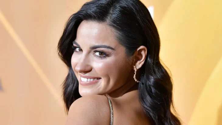 Maite Perroni turns to the camera with a smile, her back is slightly turned away