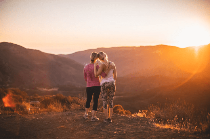 una mamá y su hija viendo el atardecer están de espaldas y abrazadas ambas llevan ropa deportiva 