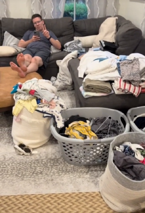 un hombre está acostado en el sofá de la sala de su casa mientras tiene mucha ropa regada alrededor