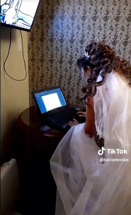 Mujer vestida de novia sentada frente a una laptop antes de ir a su boda 