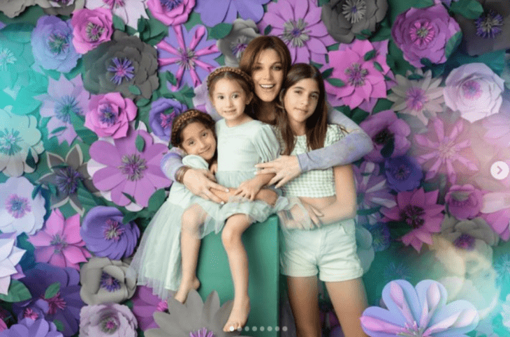 Natalia Alcocer en una sesión de fotos juntos a sus tres hijas rodeadas de flores violetas 