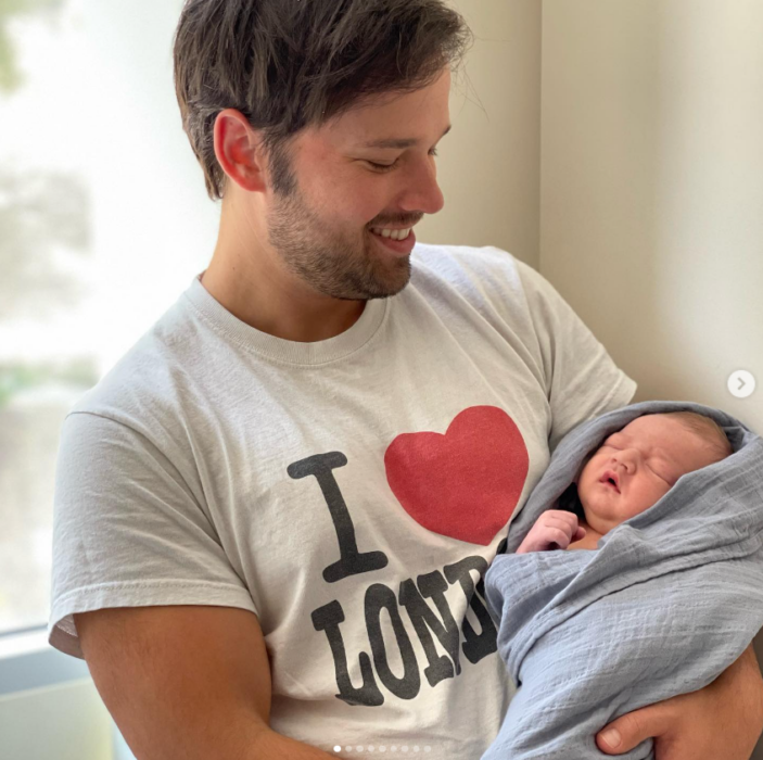 Nathan Kress cargando a su pequeño hijo recién nacido lo mira con una sonrisa