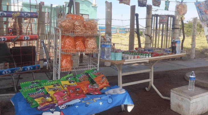 una humilde tiendita de dulces y botanas instalada en la calle conformada por un par de mesas una hielera y algunos estantes de botanas