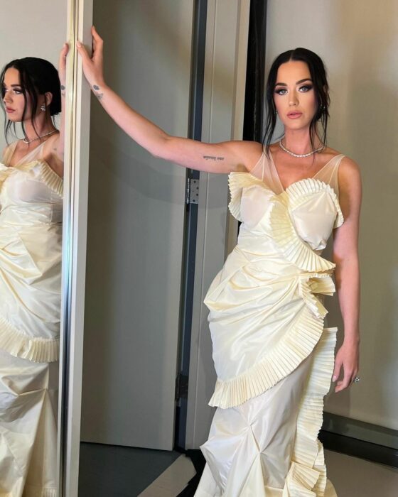 Katy Perry con vestido color perla recargada en un espejo 