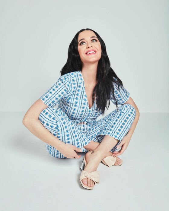 Katy Perry sentada en el suelo con un traje azul y las piernas cruzadas 