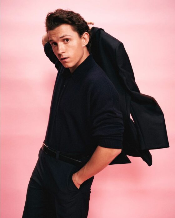 Tom Holland vestido completamente de negro en fondo rosa