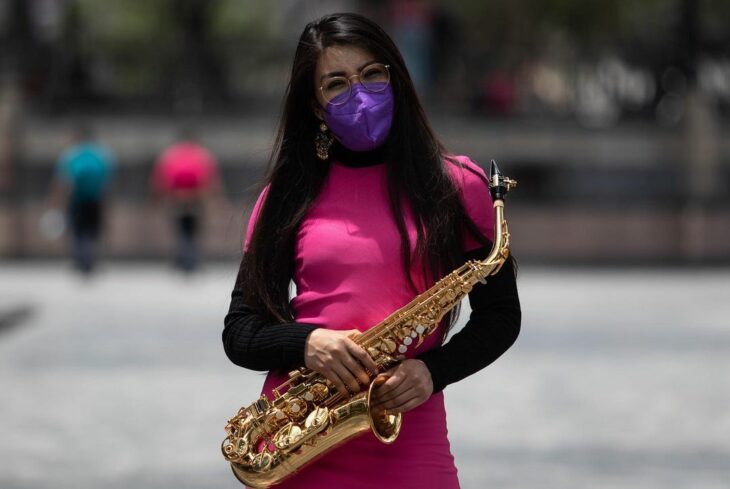 Elena Rios con su sax y vestido rosa en medio de una plaza 