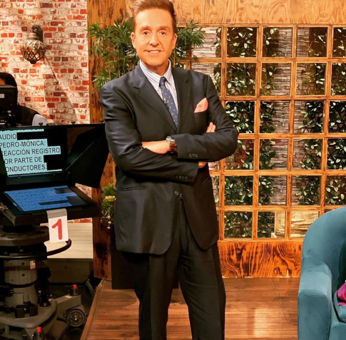 Daniel Bisogno posa de pie en el foro del programa Ventaneando lleva un traje gris con corbata azul