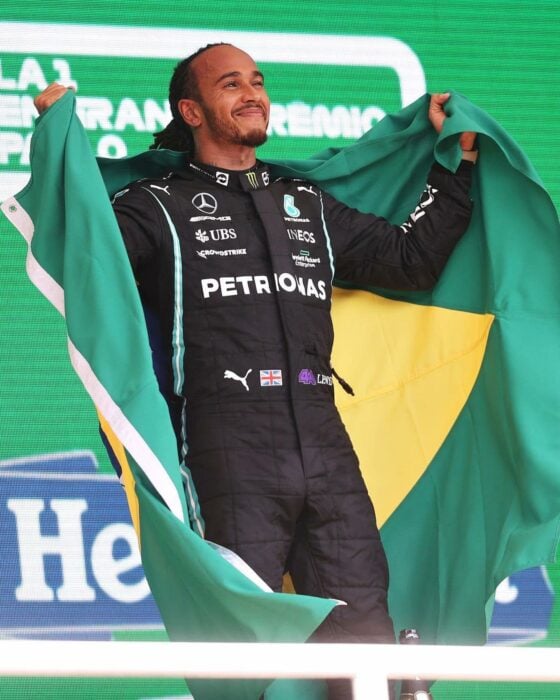 Lewis Hamilton posando en una carrera con una bandera de brasil detrás de su espalda 