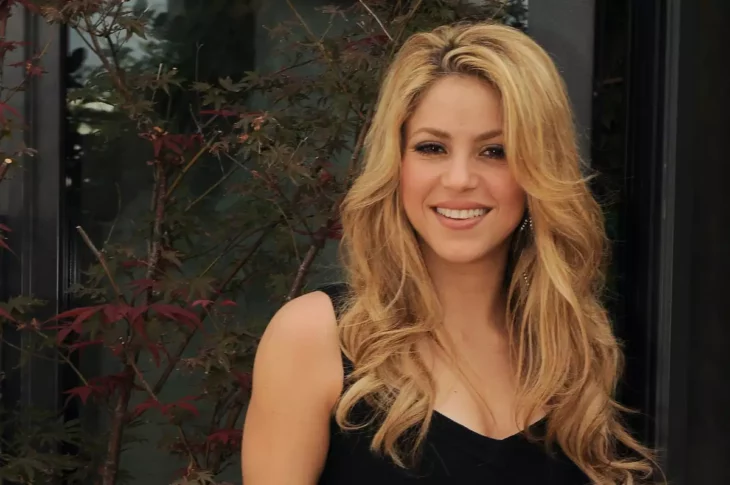Shakira posa sonriente con el cabello peinado en ondas se encuentra en un jardín exterior 