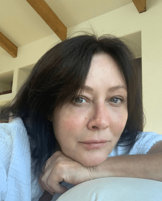 la actriz Shannen Doherty pensativa con el brazo bajo su barbilla no lleva maquillaje