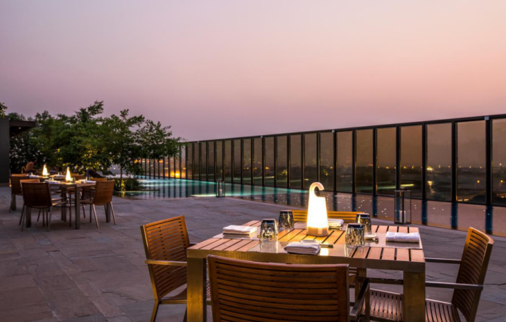 uno de los restaurantes al aire libre del Hotel Roseate House de Nueva Delhi una mesa de madera con una lámpara colocada al centro