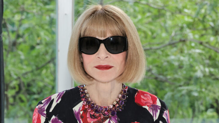 Anna Wintour posando con lentes de sol super oscuros lleva una melena corta rubia y un vestido estampado