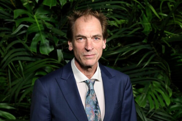 Julian Sands en exterior con traje y corbata azul