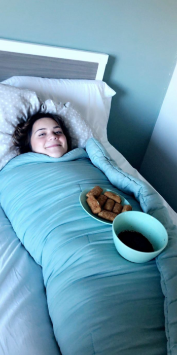 una chica esta completamente envuelta en una colcha de color azul sobre ella tiene un plato con comida y un tazón con cátsup 