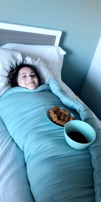 una chica esta completamente envuelta en una colcha de color azul sobre ella tiene un plato con comida y un tazón con cátsup 