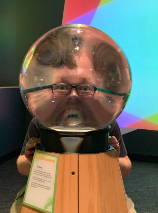 un hombre distorsionando su rostro al colocarse sobre una esfera que lo amplifica 