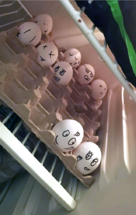 unos huevos en el refrigerador colocados en el cartón donde son transportados tienen pintadas caritas con plumón negro 