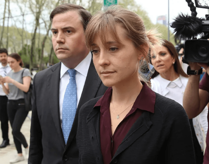 Allison Mack camina con sus abogados mientras los fotógrafos la asechan lleva el cabello recogido en un chongo y luce sin maquillaje