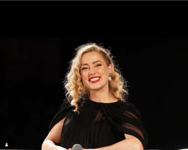 Amber Heard sonríe en la presentación de su última película In the fire lleva un micrófono en las manos y porta un vestido elegante de color negro