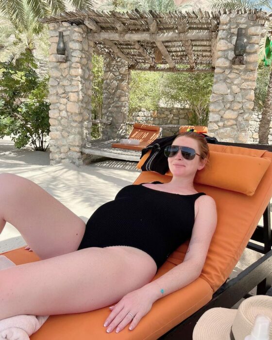 Lindsay Lohan recostada en traje de baño color negro con su barriga de embarazo 