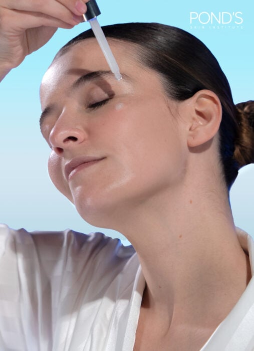 Mujer usando sérum de ácido hialurónico de Pond's para skincare con el gotero directamente en la piel